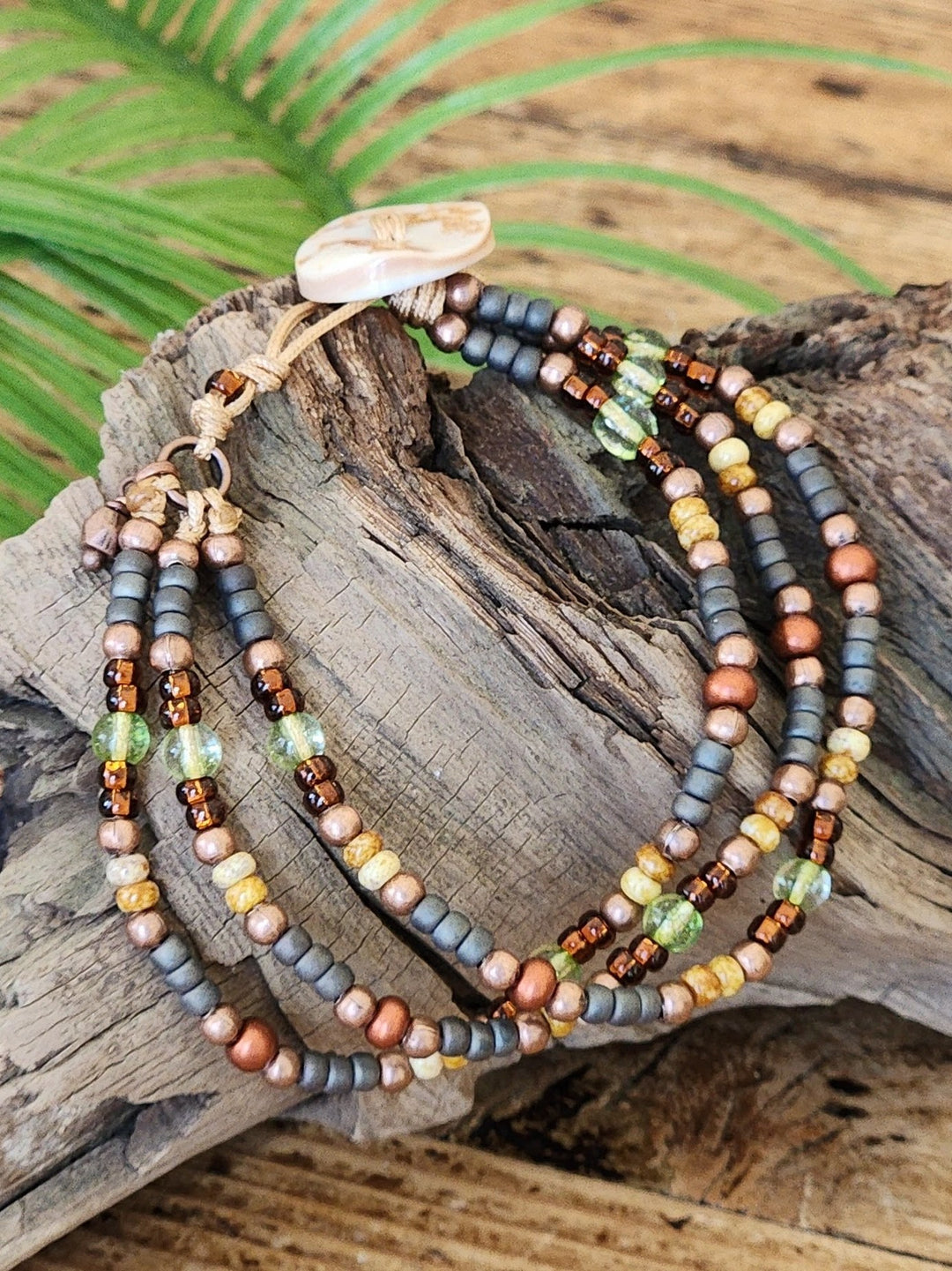 This photo showcases the brown, orange, yellow, beige, green, brown, gray and copper color pallet of the 3 Strand Crocodile Eye bracelet.