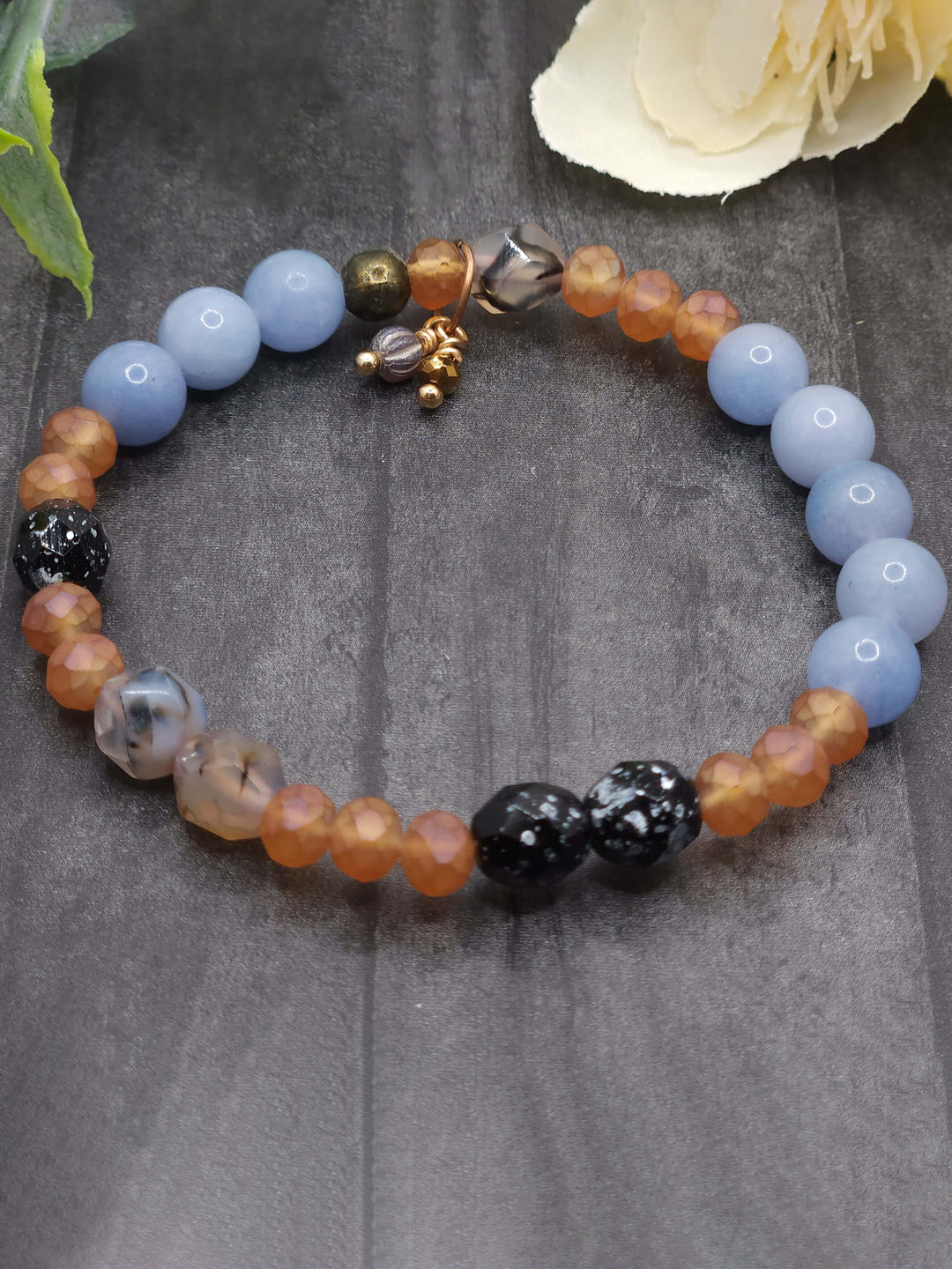 This is a photo of the American Kestral Strech Bracelet with colors of pale blue, soft orange, beige, and small touches of black. A gray Czech Glass melon bead and a small gold colored crystal are hand wire wrapped as charms.