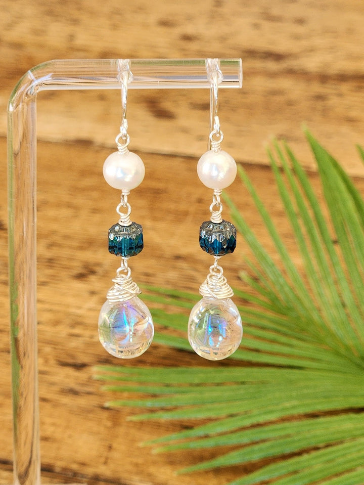 This photo shows the Jellyfish earrings with a soft brown wood background and a palm leaf as well as the iridescence and flowing nature of this magnificent Jellyfish.