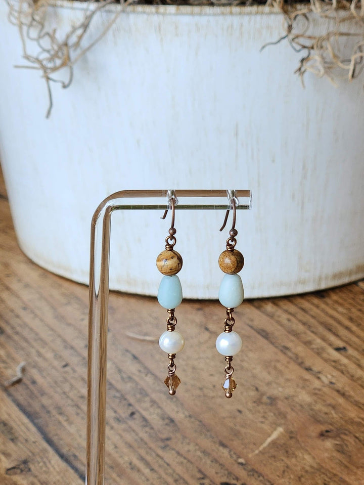 This is a photo of the Sand Dune earring on a clear display stand with soft touches of cream and brown in the background.