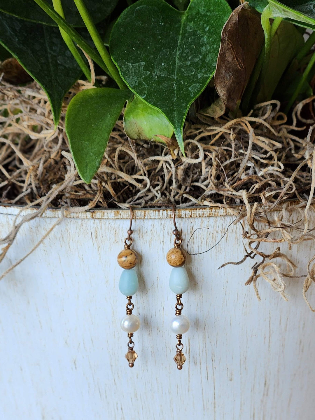 This is a photo of the Sand Dune Earrings hanging on a crean pot vase alongside green leaves.